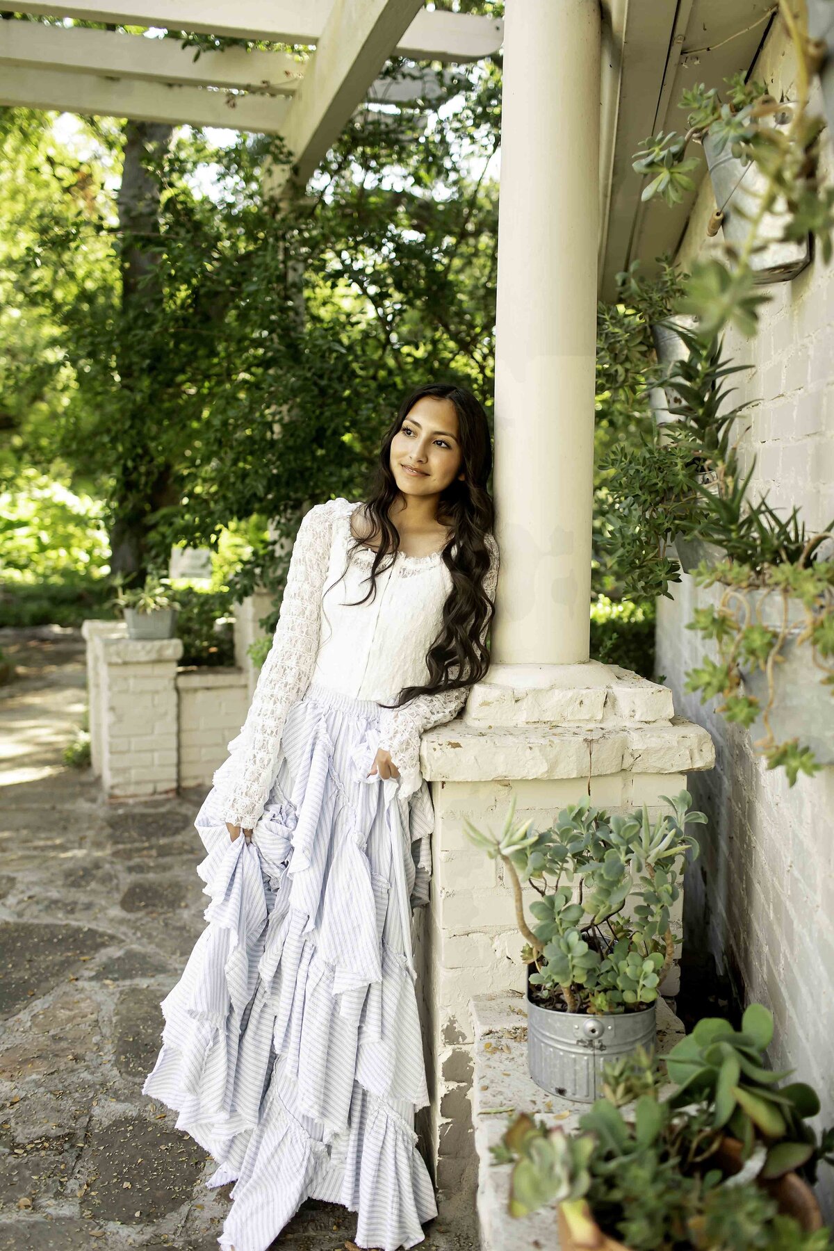 A high school senior surrounded by the vibrant greenery and elegant pathways of Chandor Gardens in Weatherford, TX, celebrating the beauty of both nature and accomplishment