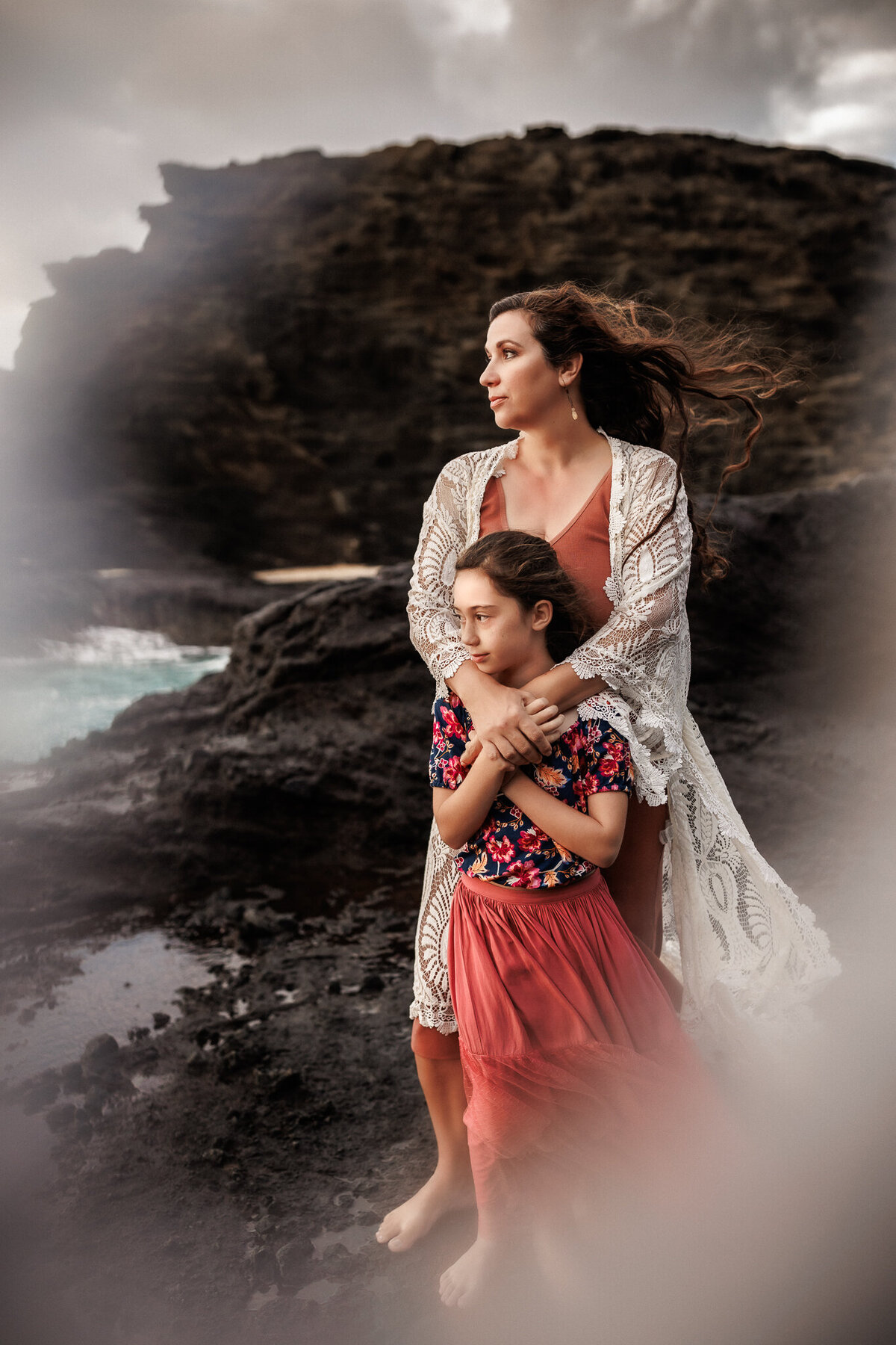 mom and daughter on rocky coast with windblown hair