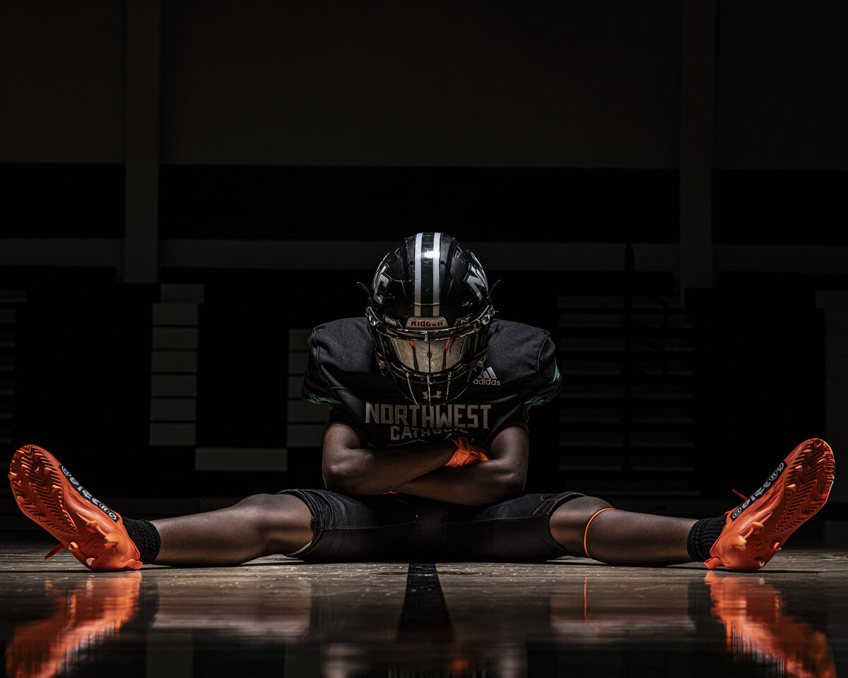 CT Photographer | Media Day Photos | Football Player Photos sitting with legs wide against a dark background. 