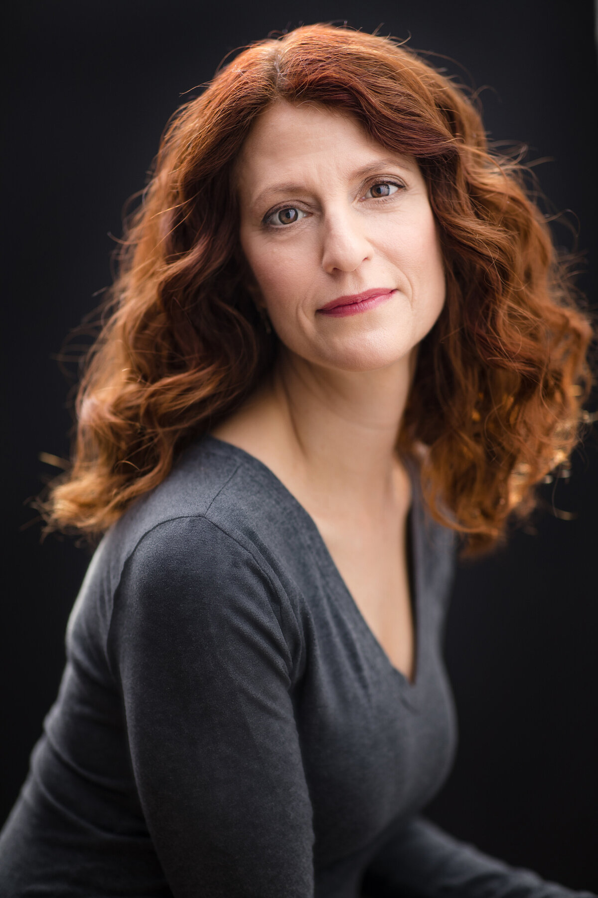 A woman with red curly hair looking to the side.