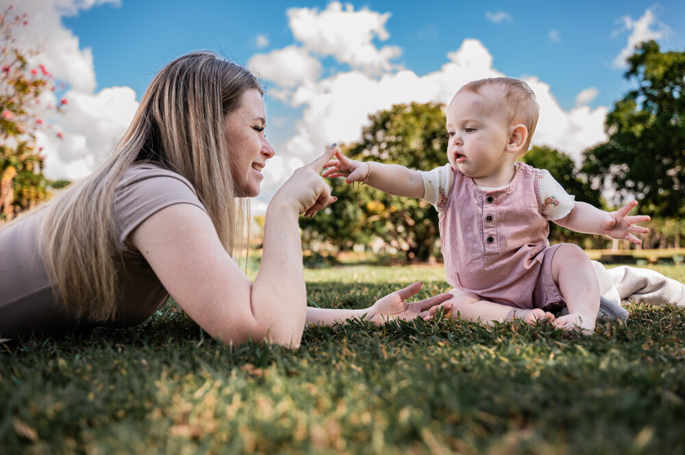 mum lying and baby sitting in a garden touching fingers - Townsville Child Milestone Photography by Jamie Simmons