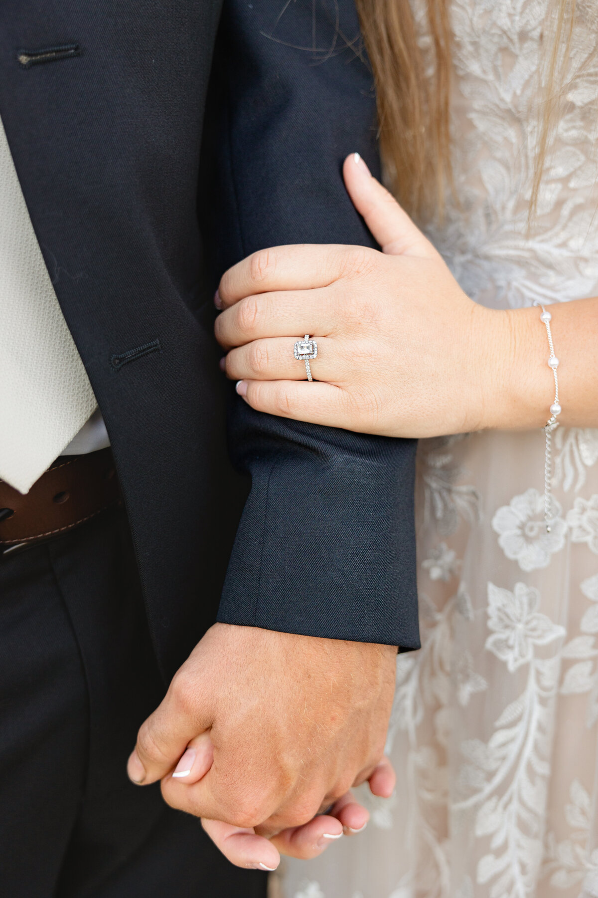 Bride rests her head on the groom’s arm, showcasing her engagement ring.