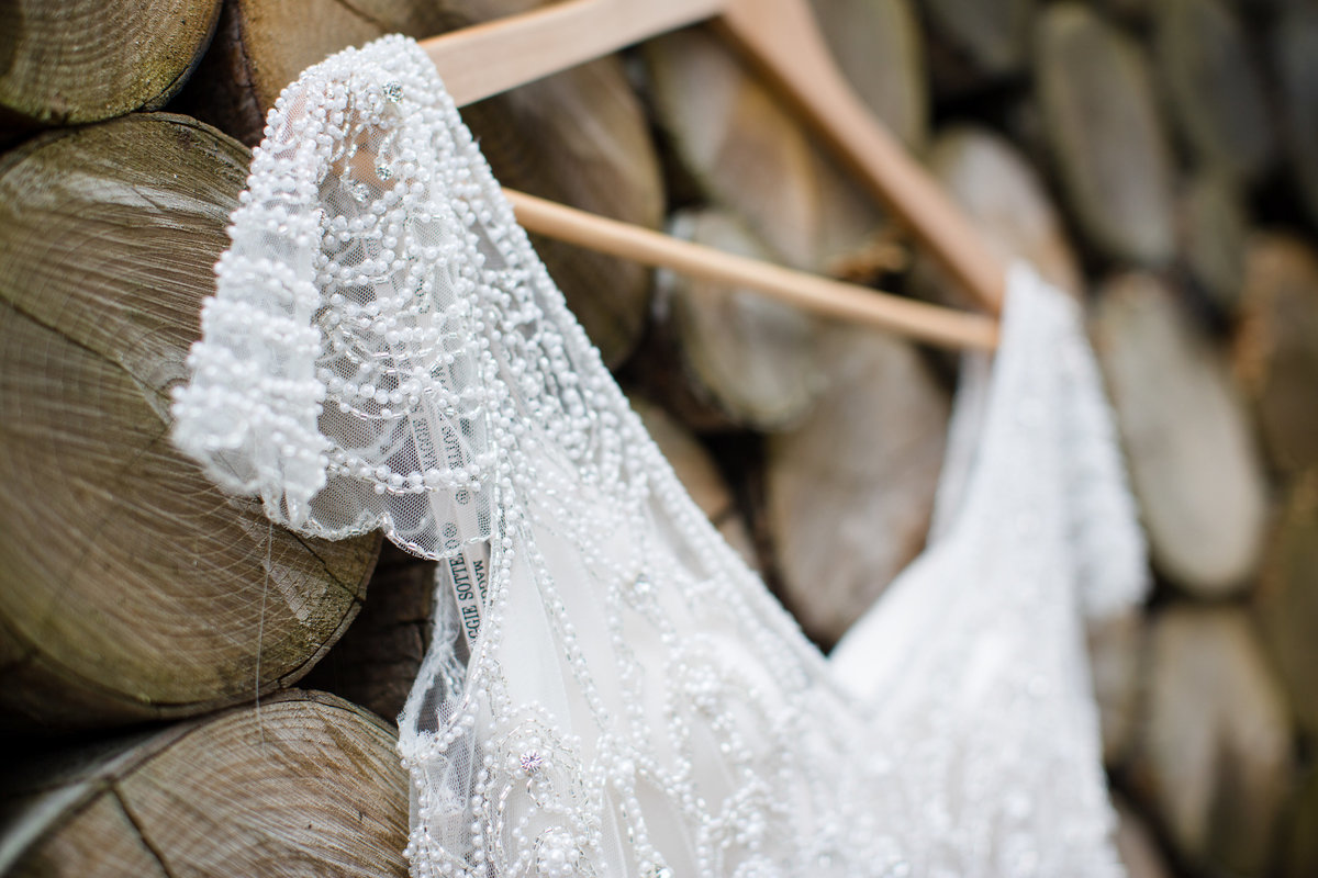 A close up of the fine beading and details of this stunning Jenny Packham  wedding dress at Southend Barns hanging on the log wall in the garden on this wedding day.