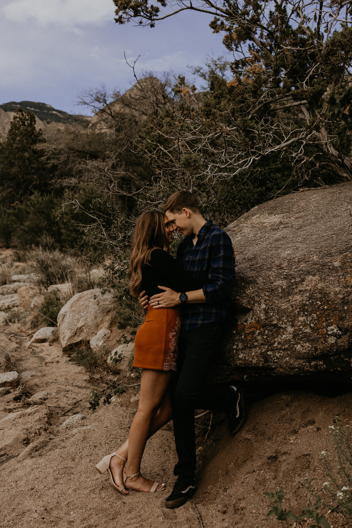 engaged couple leaning against a rock holding each other