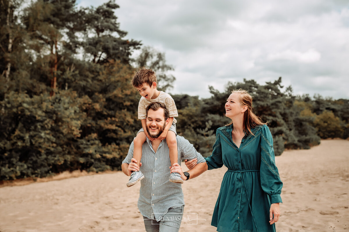 Zoon zit op de schouders van zijn vader en mama loopt erlangs en lachen samen door de duinen van de Bedafse Bergen in Uden