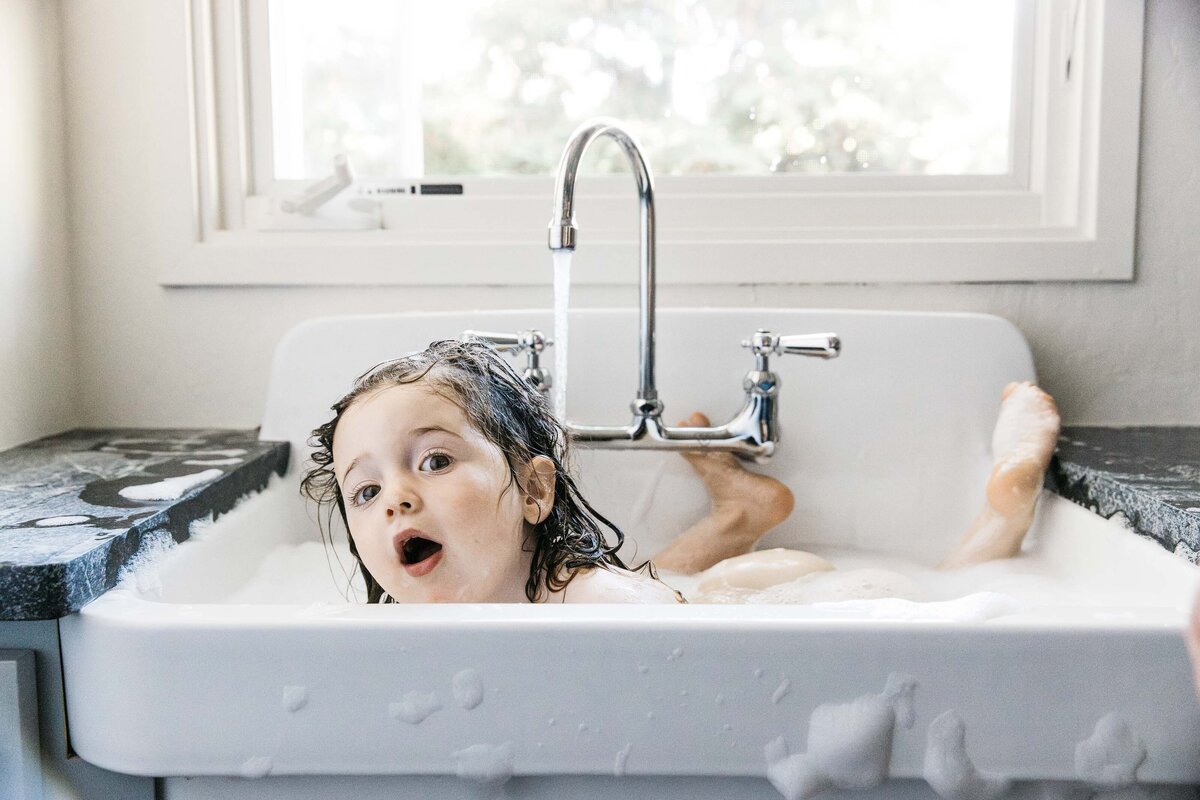 Toddler is having a bath with bubbles in the sink.