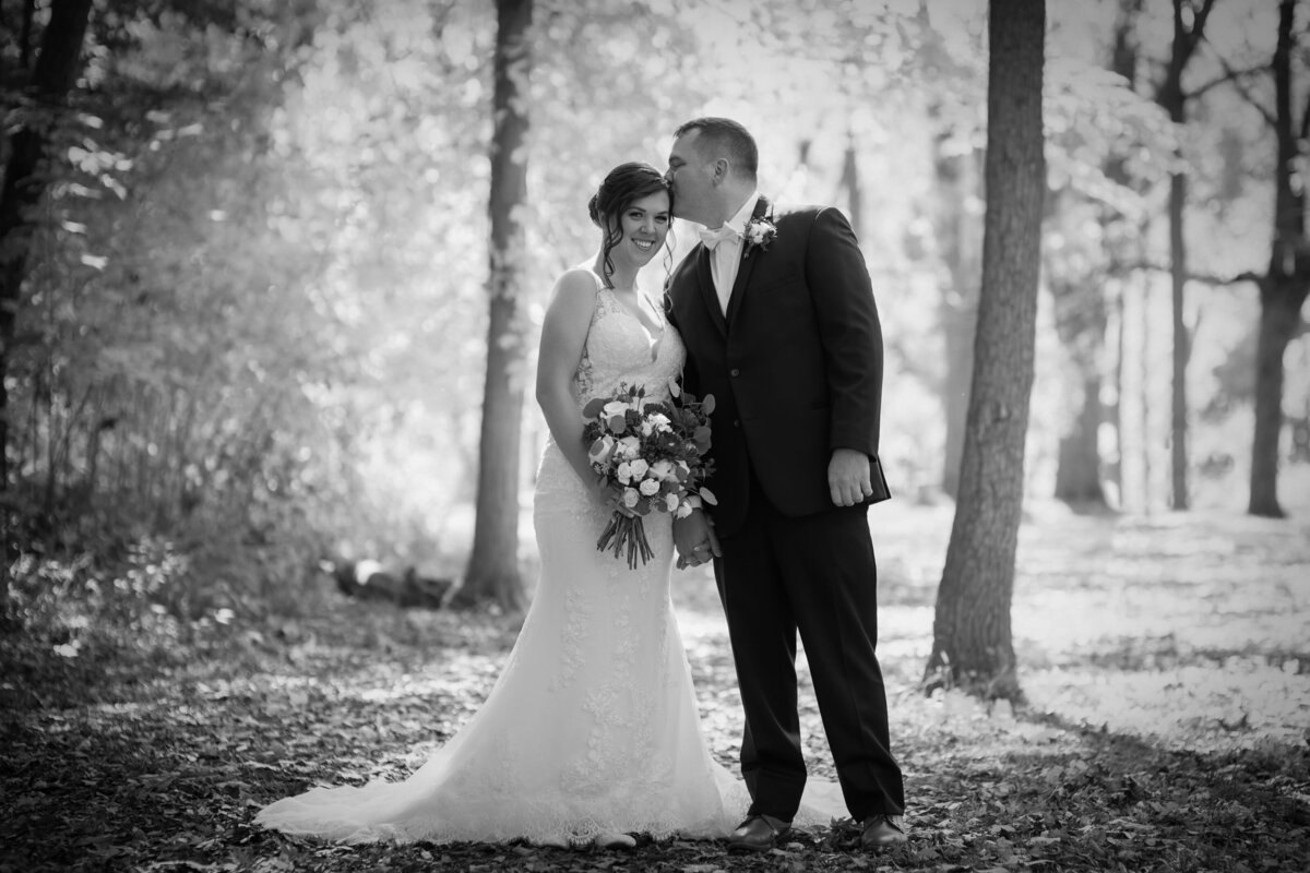 Groom kisses his bride's forehead as she smiles on their wedding day