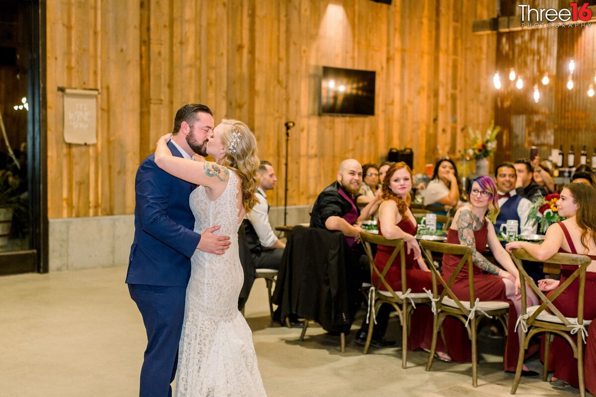 Bride and Groom share a kiss during their first dance as wedding guests look on