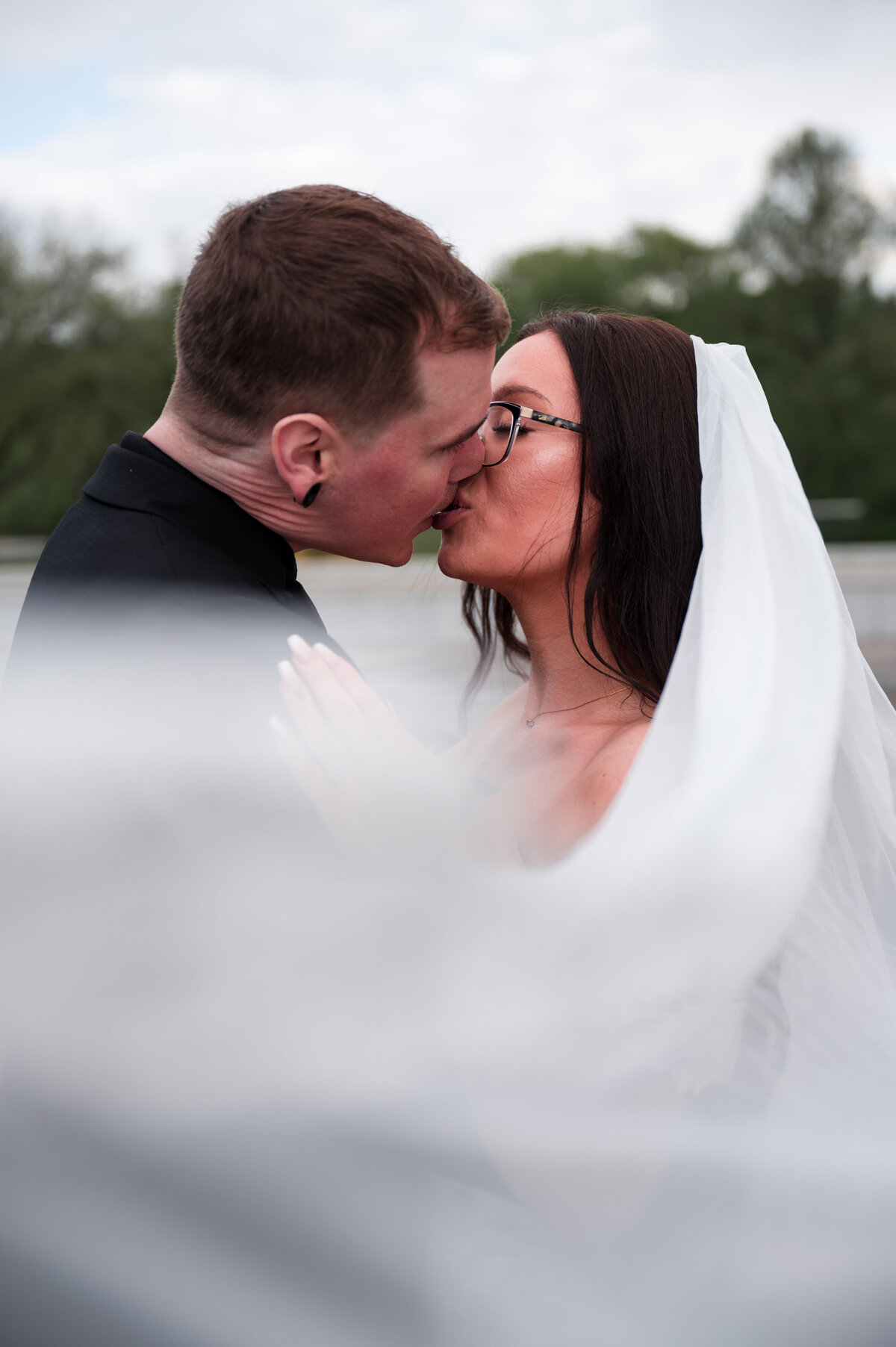 Bride and groom kiss, veil is wrapped around them creating a romantic frame