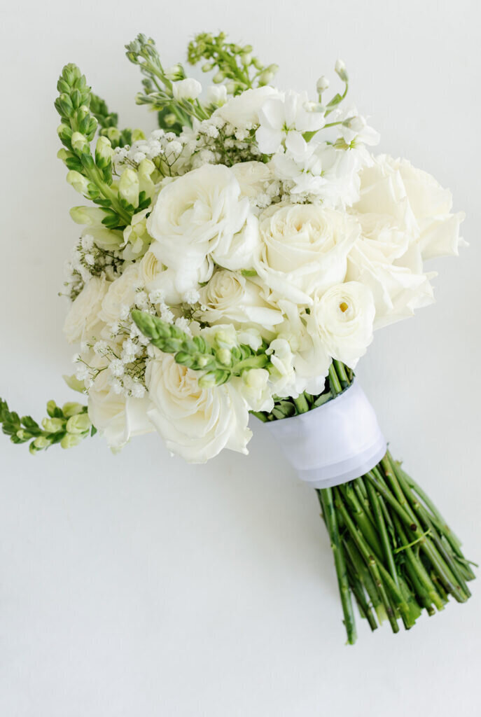 A timeless bridal bouquet featuring lush white roses, delicate florals, and fresh greenery, wrapped in a satin ribbon. Captured by Claudia Amalia Photography, a destination wedding photographer in the Florida Keys.