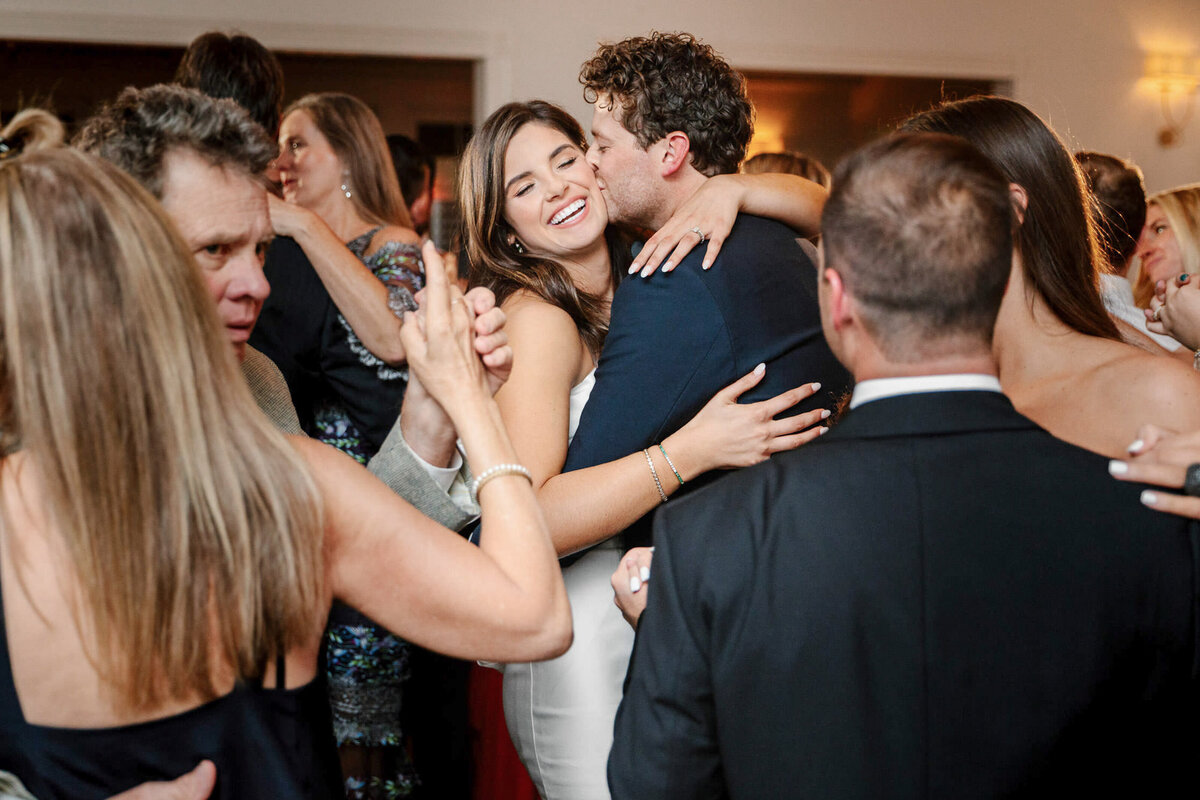 groom kissing laughing bride while dancing with wedding guests