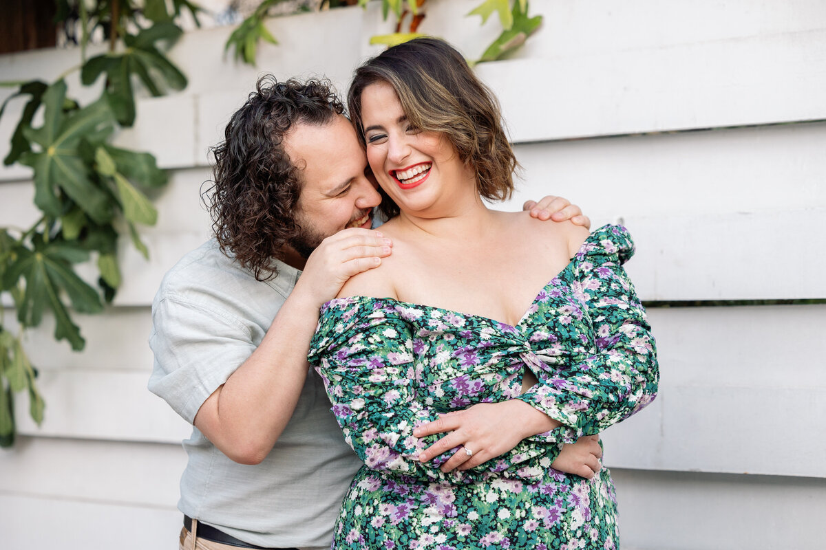 A person standing behind their partner leaning in as they both smile