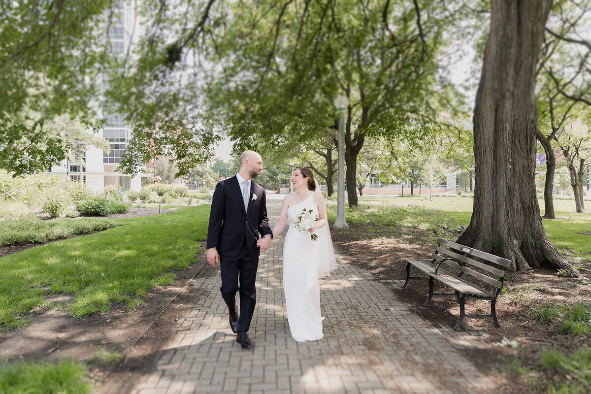 couple walks through sun dappled walkway in a park, holding hands and laughing