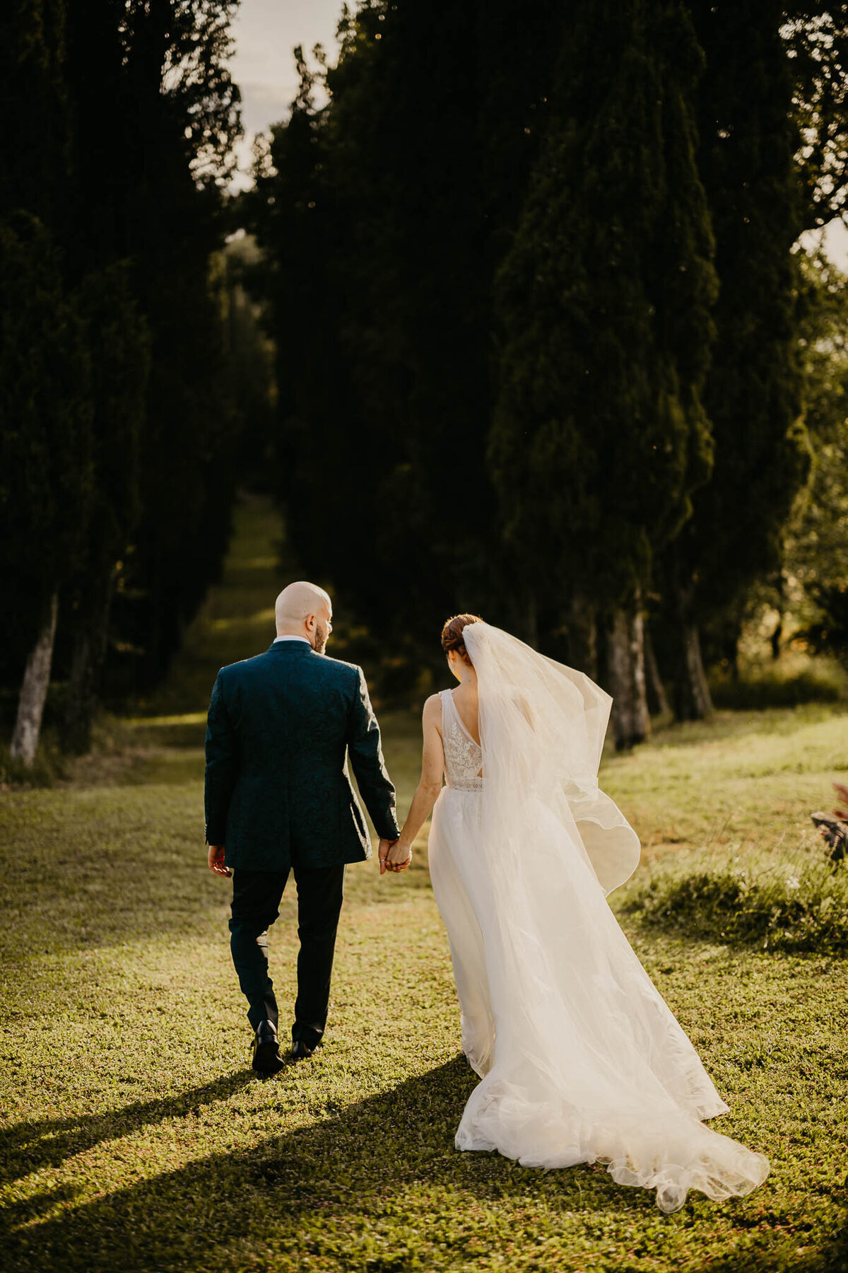 Bride and groom walking hand in hand among cypress trees at villa Bivigliano, wedding photographer Tuscany.
