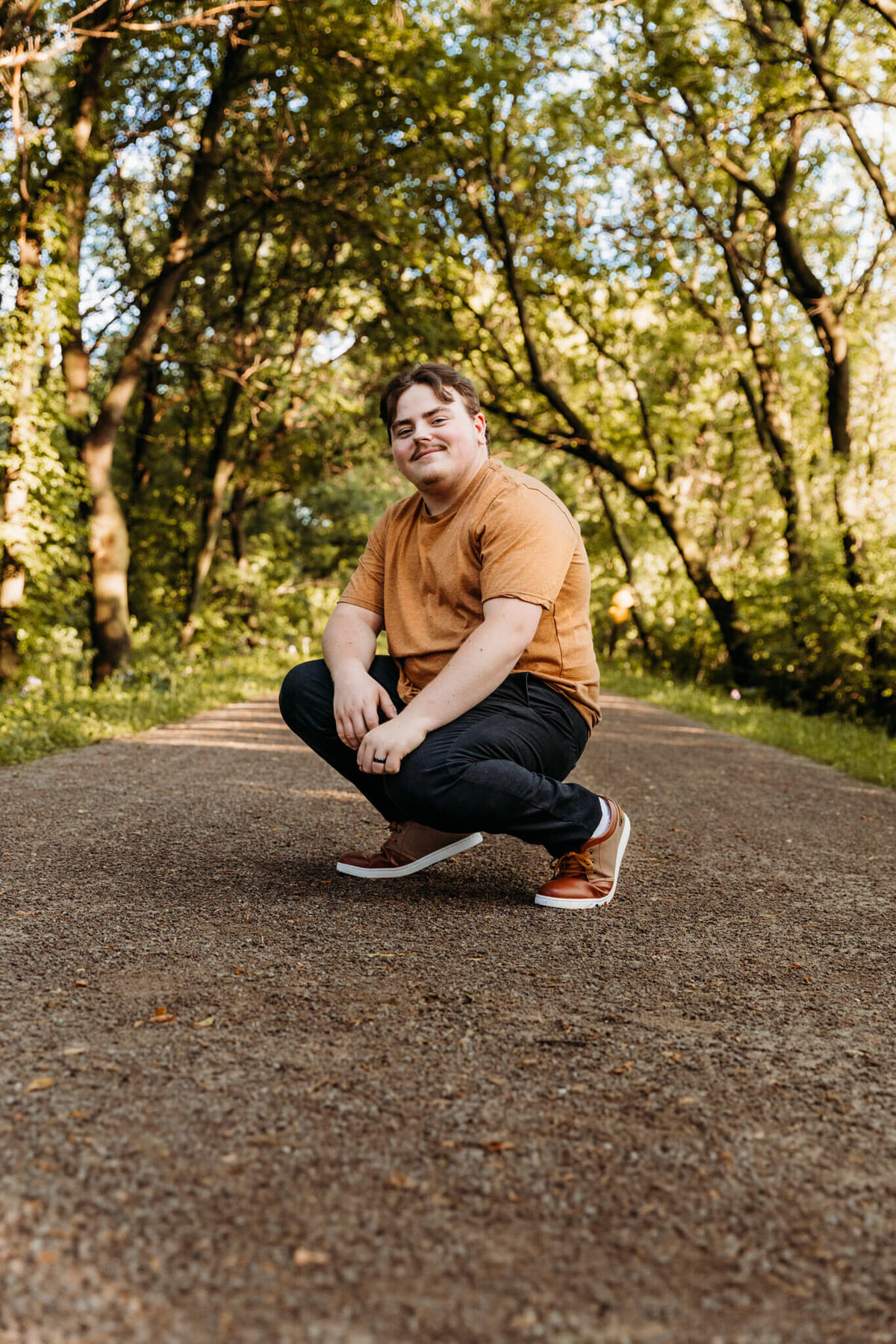 teen boy squatting on a tree covered path near Oshkosh