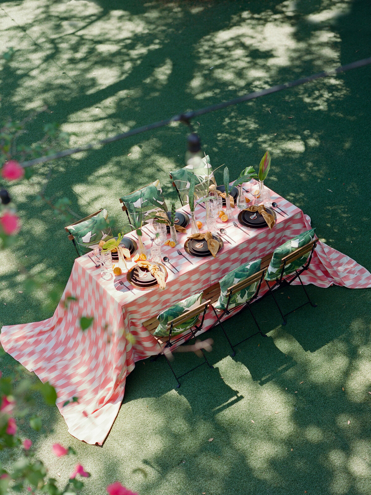 Aerial Tablescape with this blurry effect checkered red and white pattern, tropical floral accents and simple chairs with tropical themed green leaf pillows