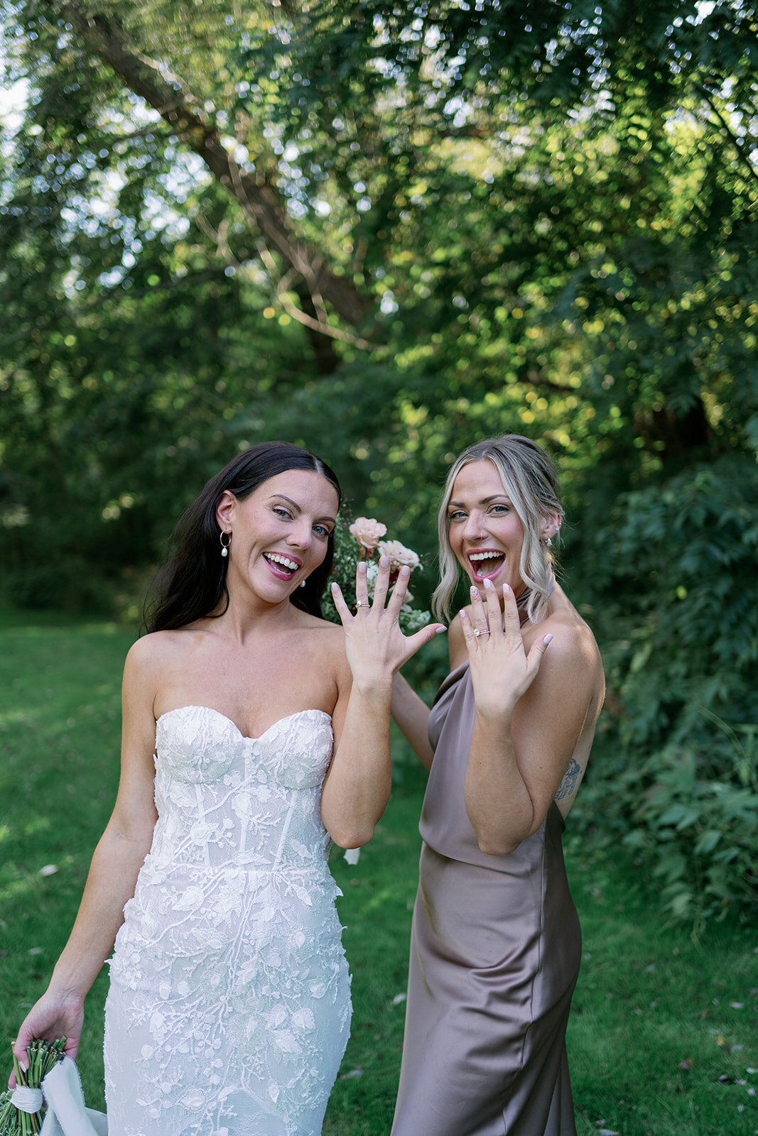 Bride and bridesmaid showing their rings in the garden at Glasshouse Community after the ceremony during a Michigan summer wedding.