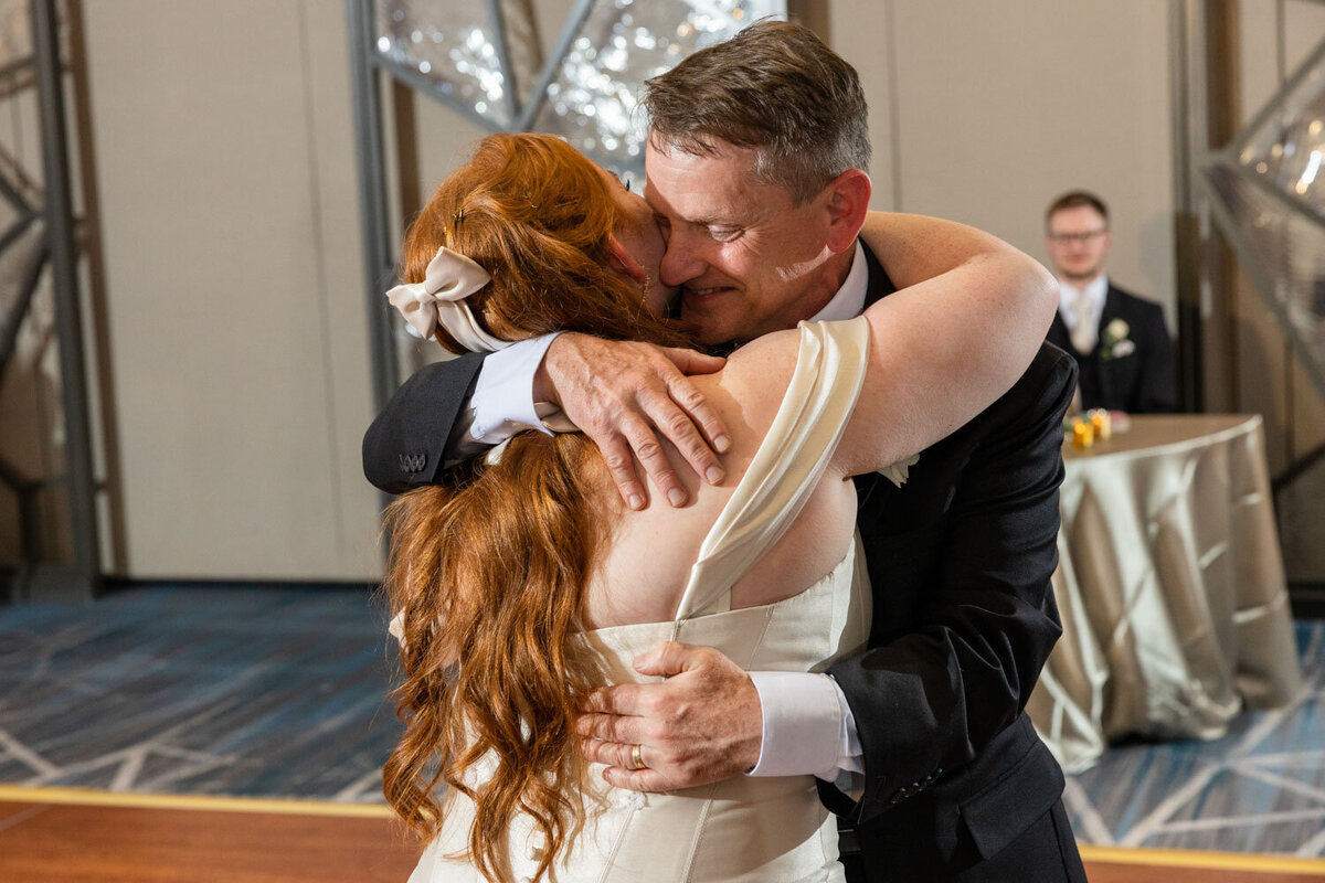 A man in a suit is hugging a woman in a white dress