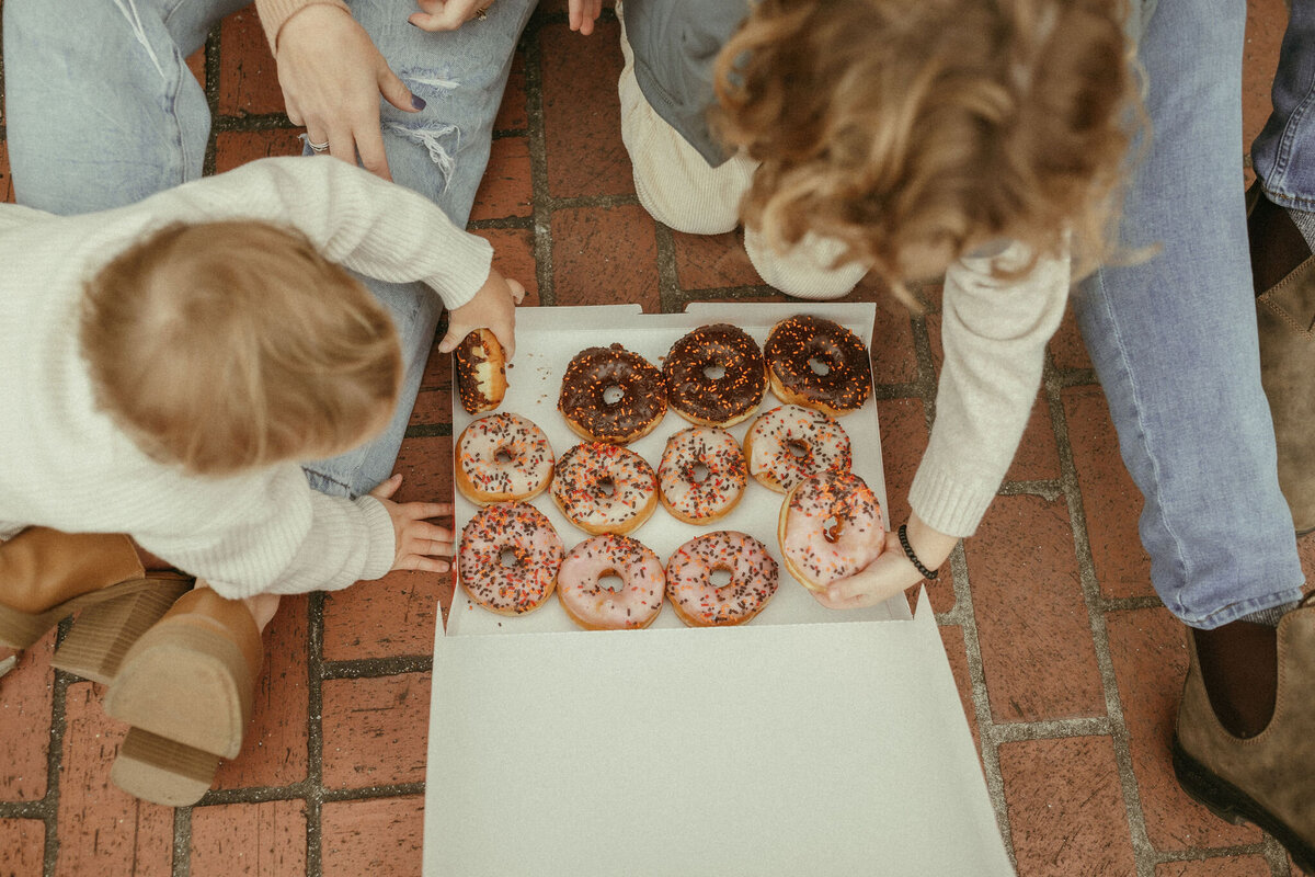 A family reaches in to a box of sprinkled doughnuts to grab their favorite flavor. 