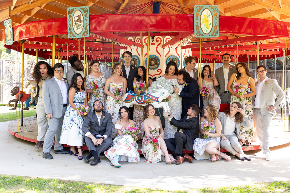 A newlywed couple and their wedding parties sitting on a merry go round