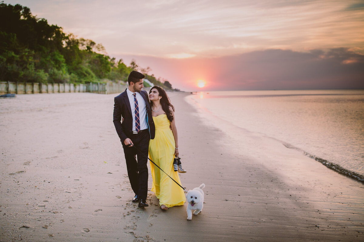 A couple walking along the shore with their white poodle dog at sunset at callahans beach in long island ny