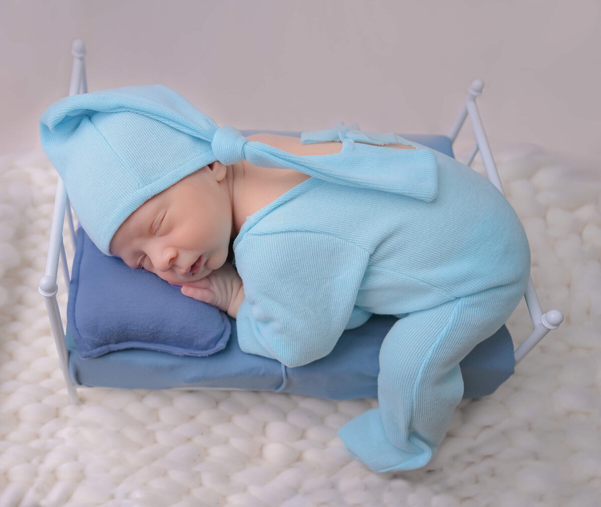 E.Benecki Photography photographed newborn dressed in blue sleeping on a white tiny bed with cream color backgrounds