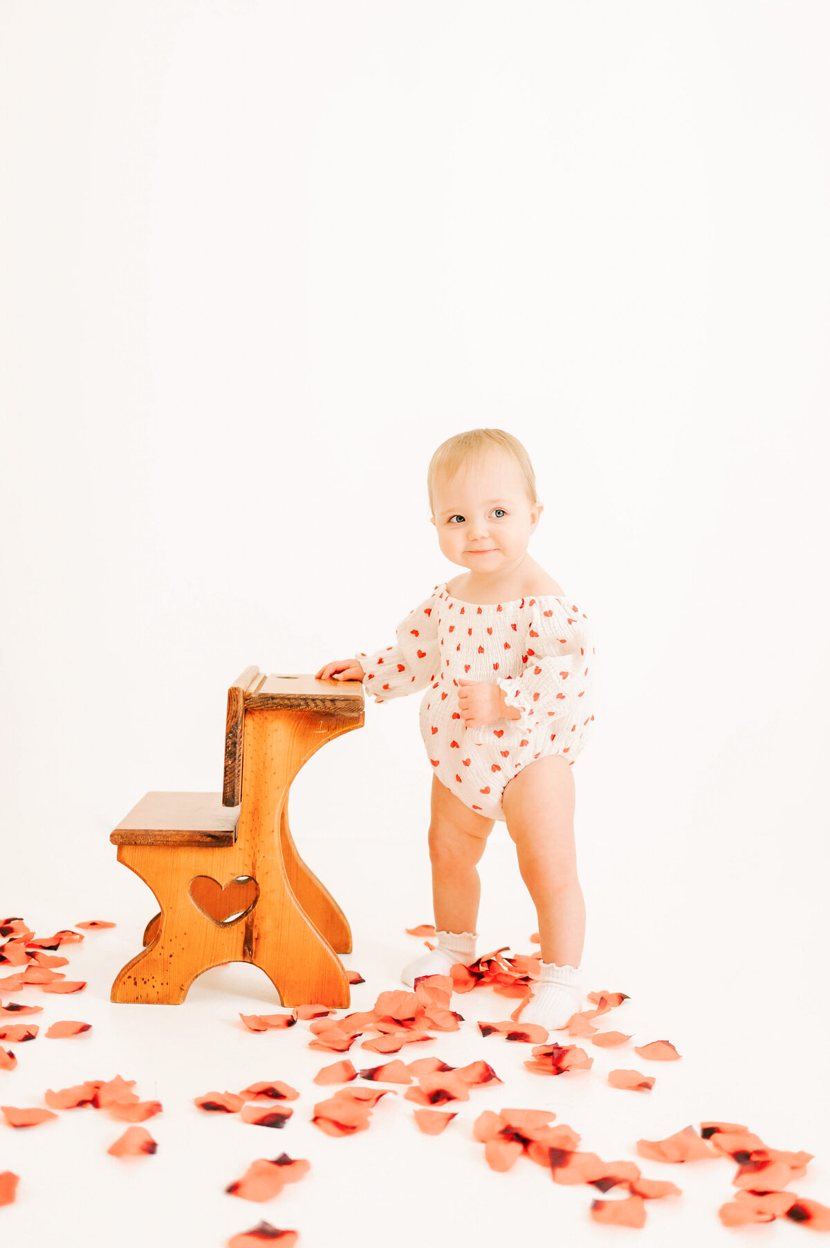 Springfield MO kids photographer captures 1 year old baby girl standing by stool smirking in photography studio