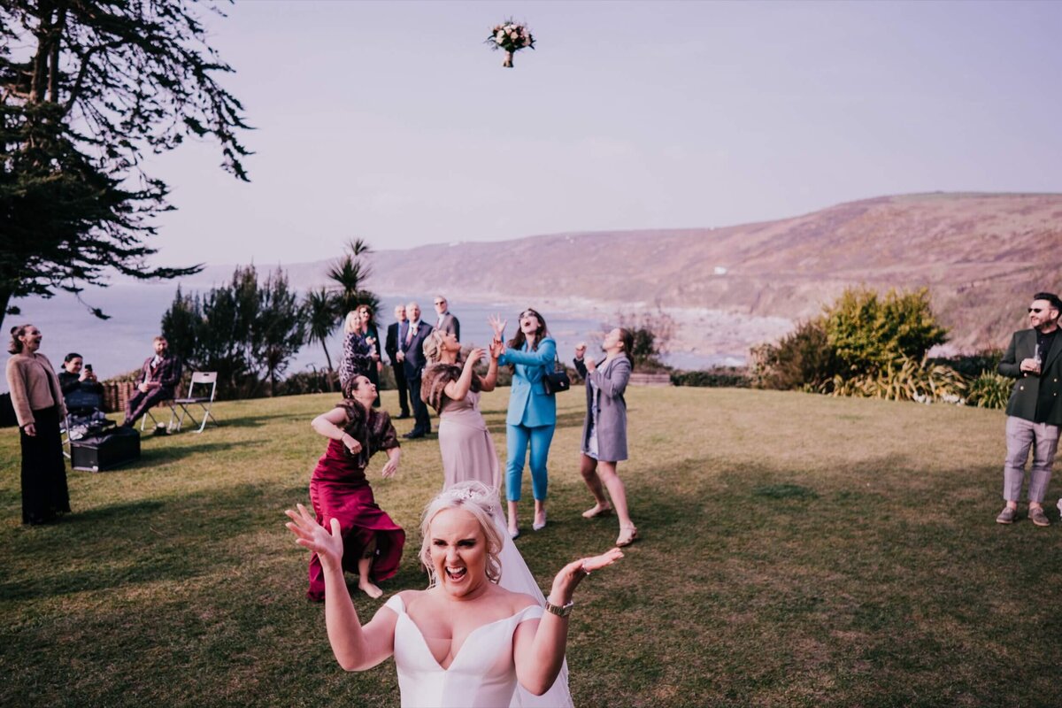 The bride throwing the bouquet on the lawn with four ladies standing behind her ready to catch the bouquet.