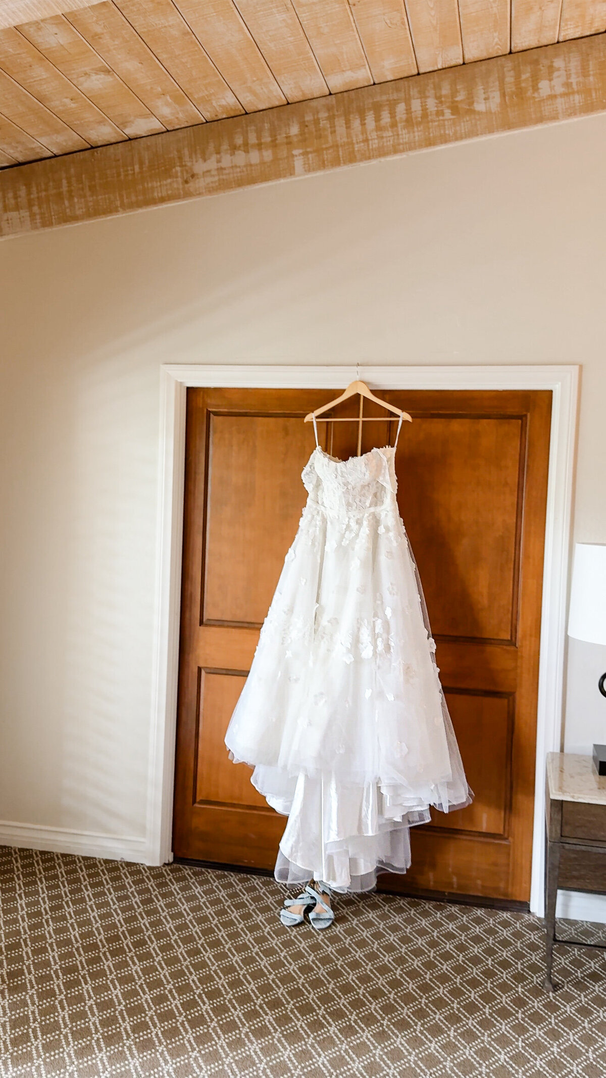 Designer, floral applique wedding dresses with sleeves and a bow hangs from a doorway in front of a brown door.