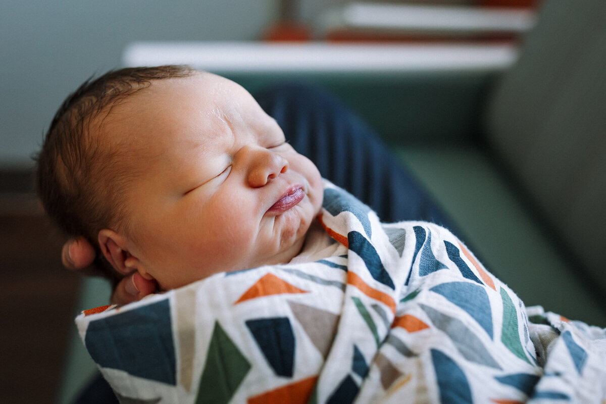 newborn scrunching his face while dad holds him in a patterned swaddled blanket