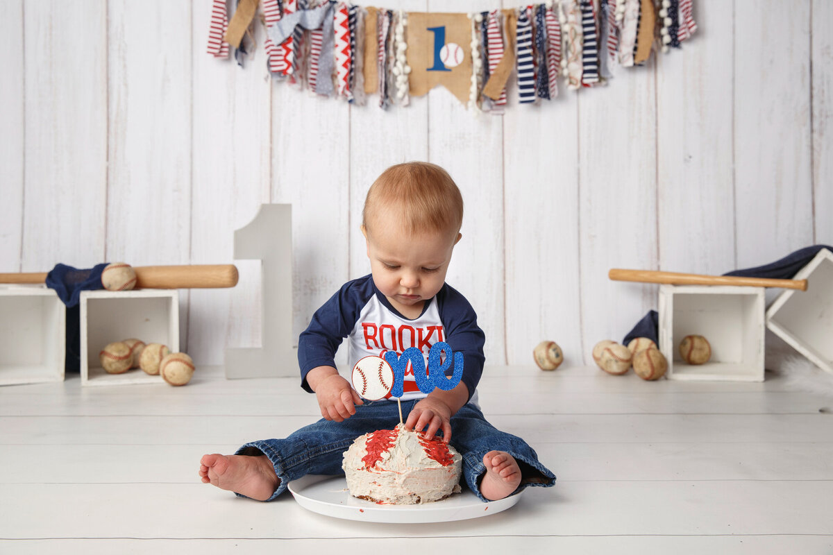 Portrait of a one year old wearing a baseball shirt with a cake and baseball themed background