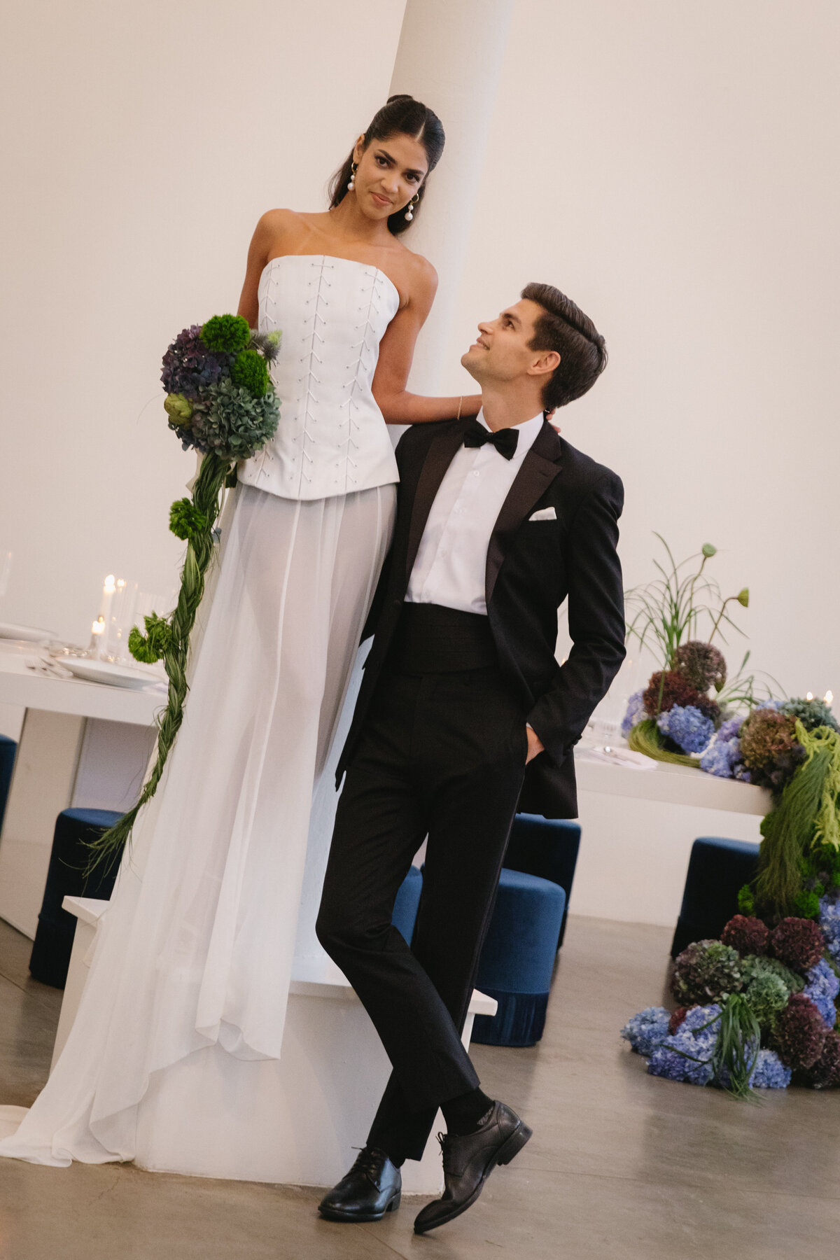 Bride and groom posed beneath soft architectural draping in a chic, minimalist ceremony space.