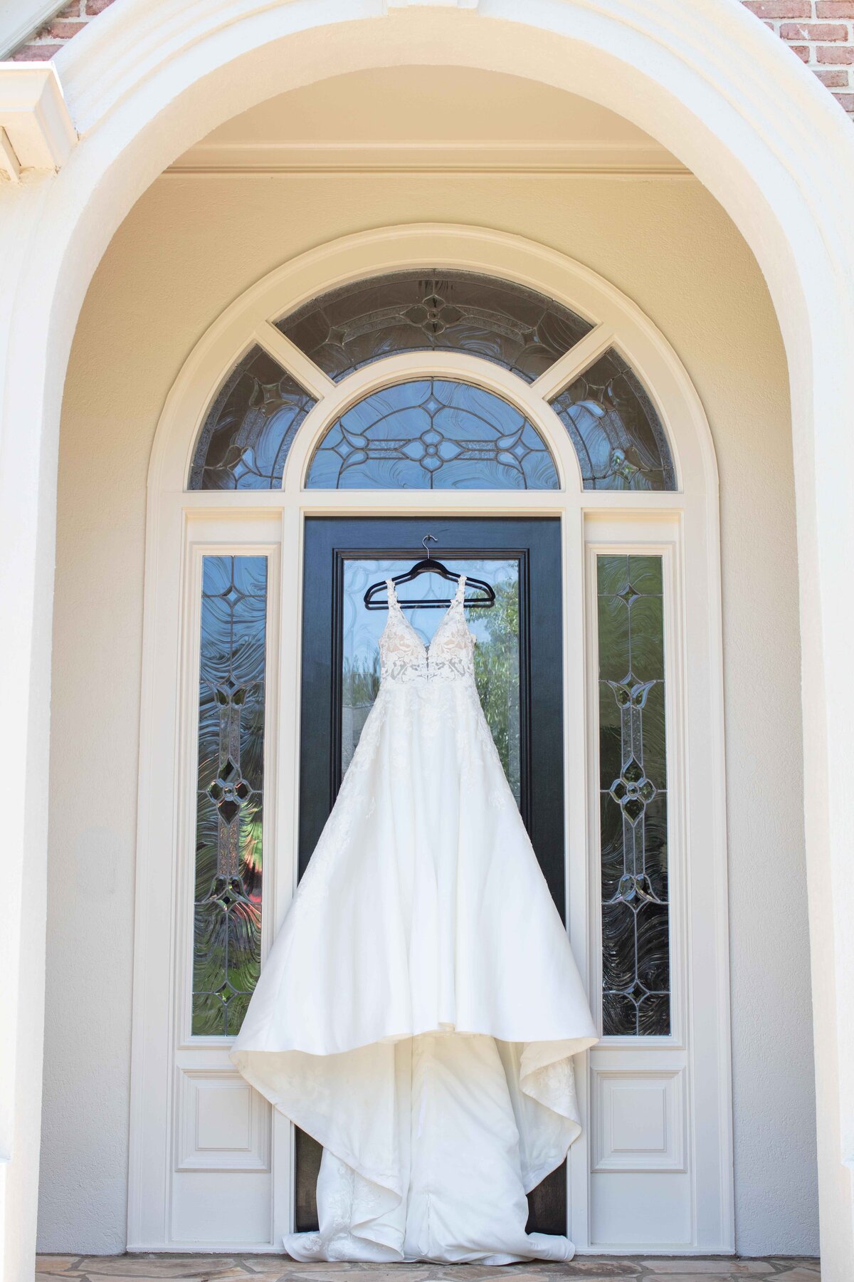 strappy wedding dress hangs on arched glass door by Firefly Photography