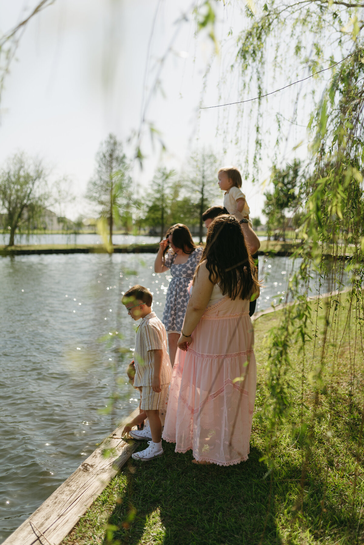 a family standing near a pond surrounded by willow trees