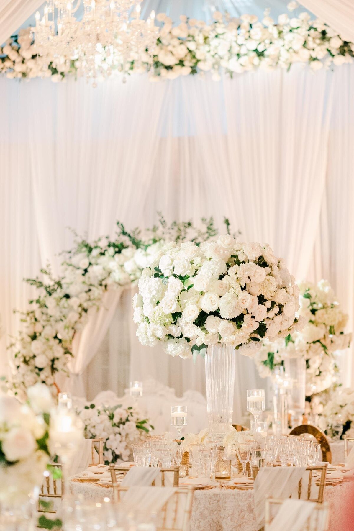 An elegant wedding reception setup with white floral centerpieces and draped fabric.