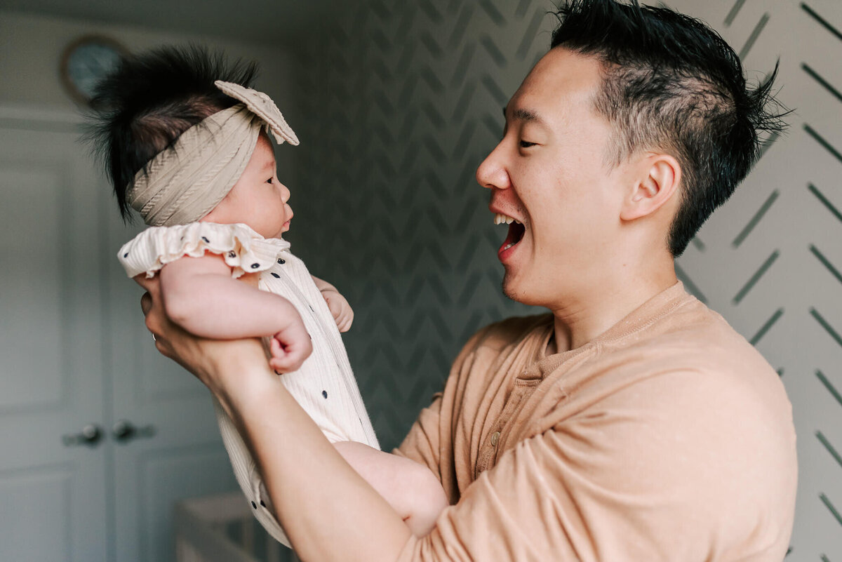 A dad having a fun moment with his newborn daughter during their session with a northern virginia in-home newborn photogrpaher