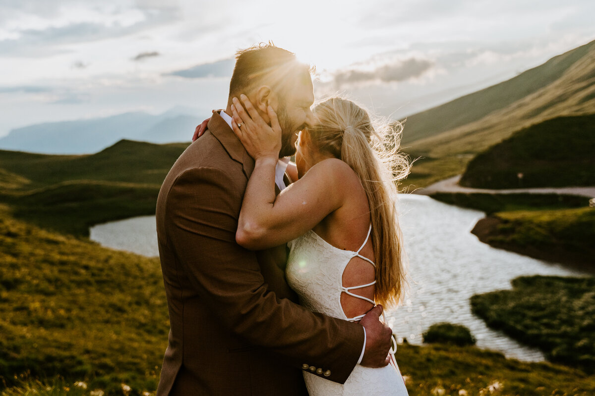 Bride and groom holding each other by alpine lake at sunset