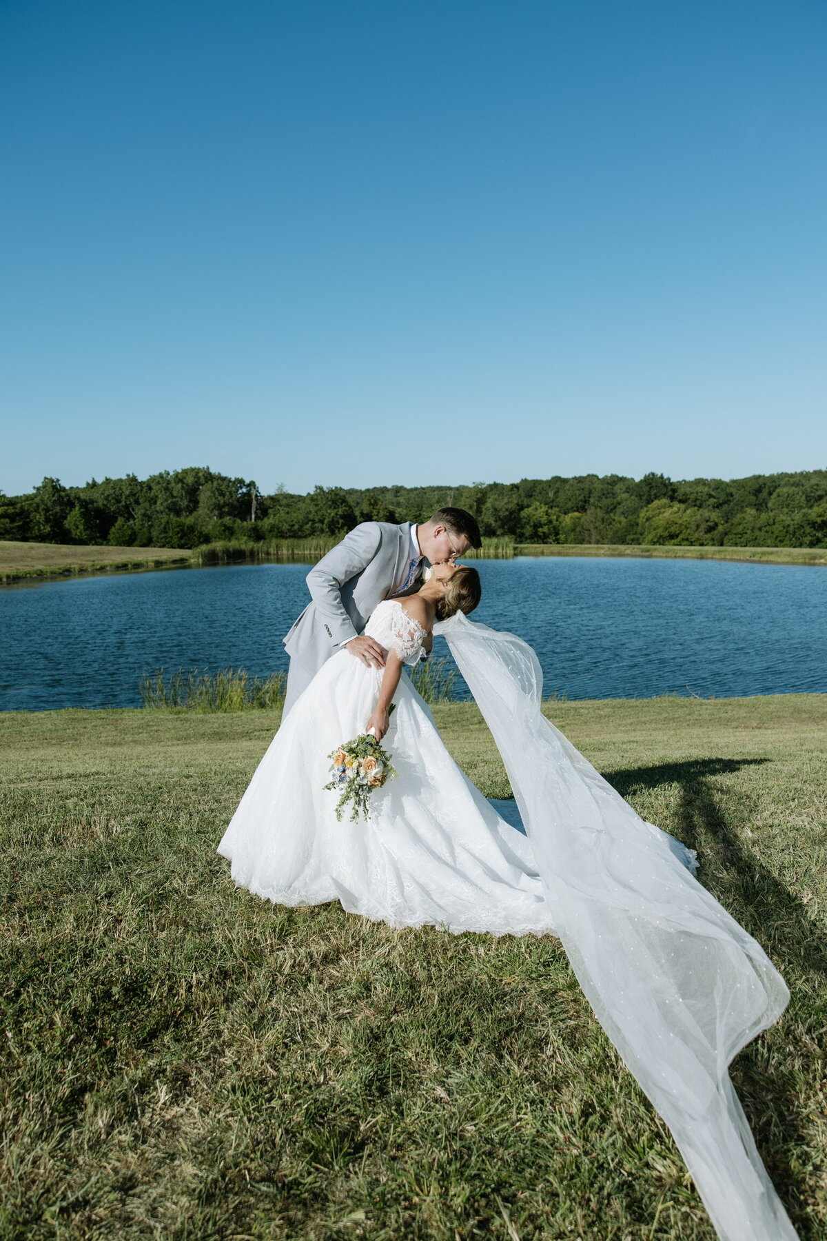 Bride and groom kissing in front of waterside pond at Willstone Acres wedding venue in Central Kentucky