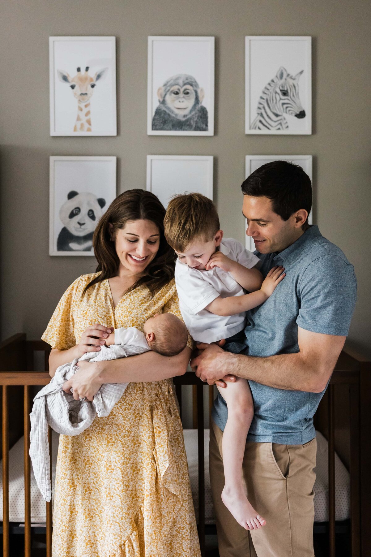 Family with two young children in a nursery, surrounded by framed animal portraits on the wall, captured by a Pittsburgh newborn photographer.