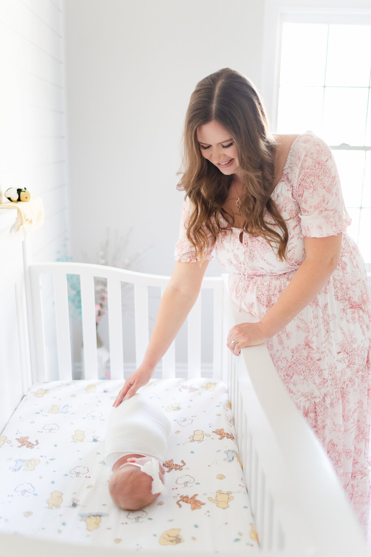 A mother at her DC Newborn Photography photoshoot reaching down to her newborn daughter in their Winnie The Pooh themed crib
