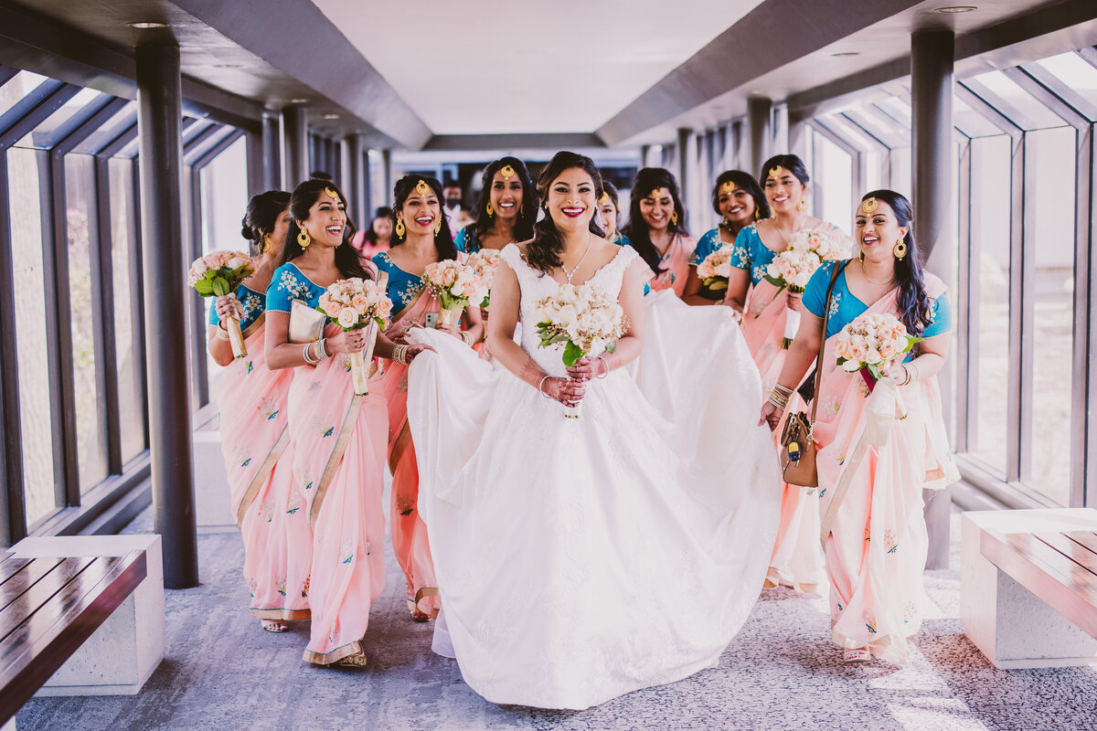 Indian christian malayali bride walking out the hotel with her bridesmaids carrying her train behind her sharing a laugh