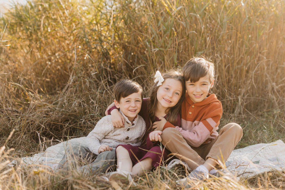 3 children snuggle together smiling  in the autumn sunlight