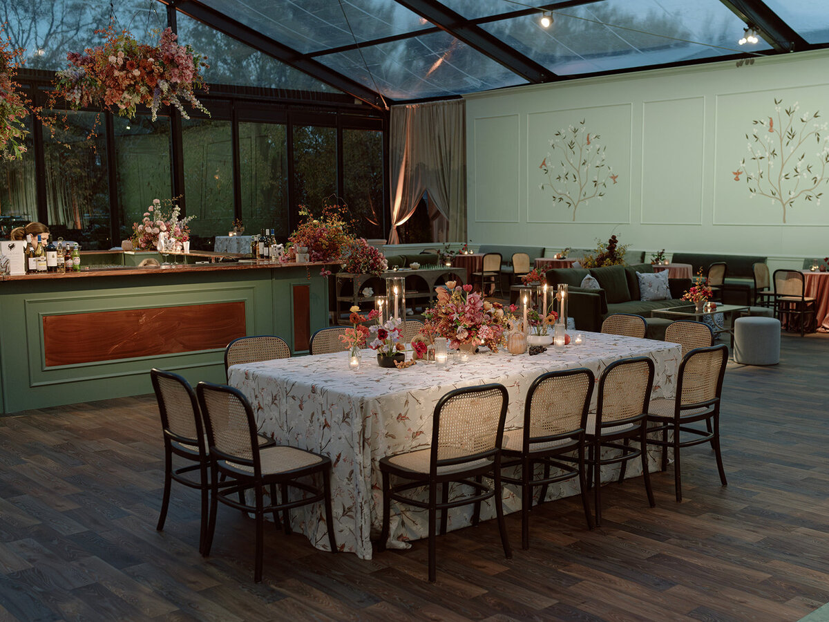 Clustered and styled floral arrangements, fruits, and art pieces for fall wedding reception. Low centerpieces mixed with ikebana arrangements and bud vases decorate the reception tables at this fall wedding. Floral centerpieces featuring orchids, ranunculus, sweet peas, and bittersweet. Styled wedding tables with fruits, curated candles, and floral arrangements. Tasteful fall color palette of copper, ruby, gold, burgundy, rust, and lavender. Design by Rosemary & Finch Floral Design in Nashville, TN.