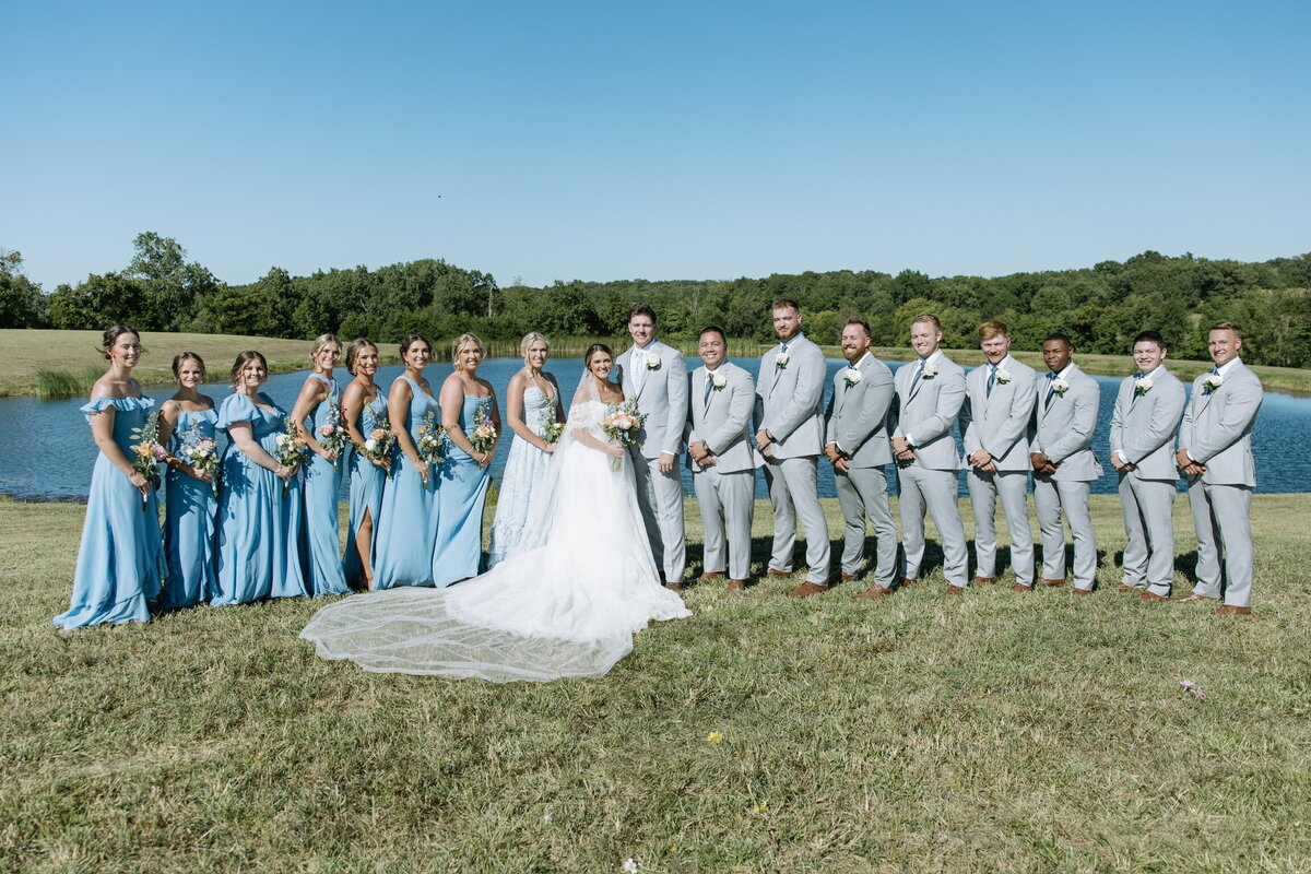 Bridal party poses in front of outdoor water pond ceremony site at Willstone Acres wedding venue