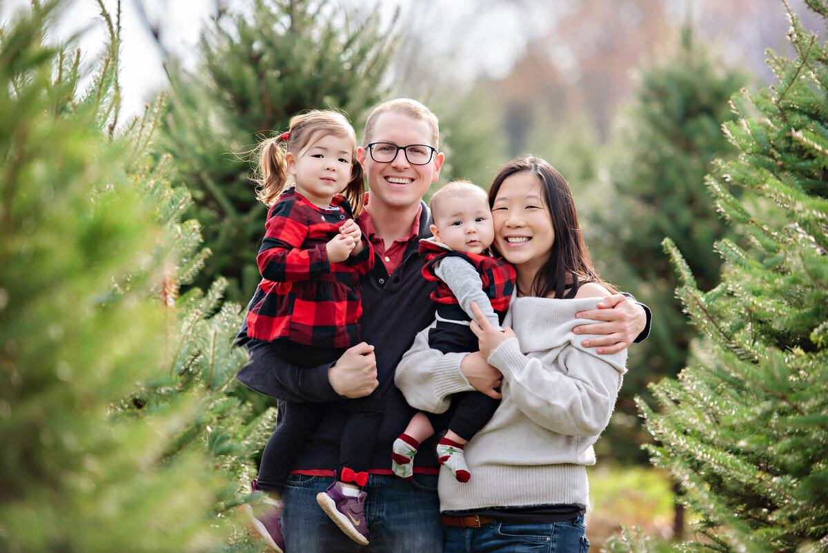 mom and dad holding their son and daughter at the Tree Farm for their Christmas family photography session in Burlington, ON