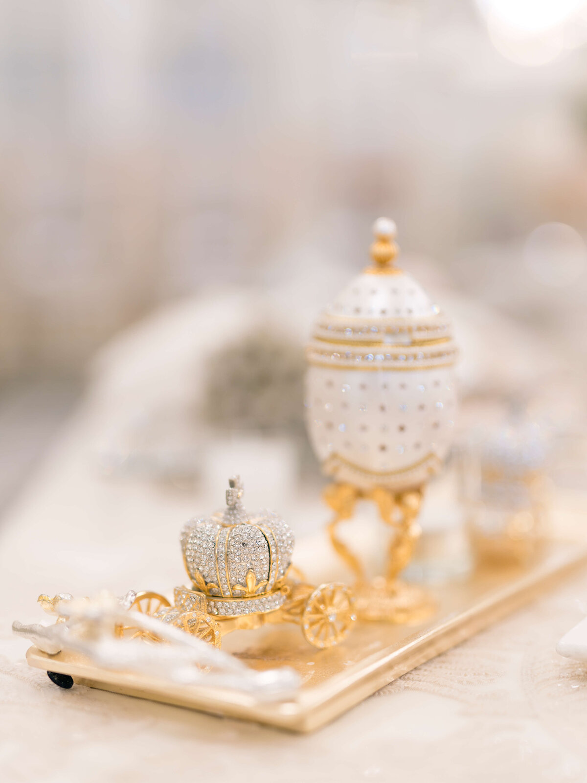 A decorative miniature coach adorned with gold and crystal accents, resembling a Fabergé egg design, on a shiny rectangular base. The intricate details highlight its elegance and craftsmanship.