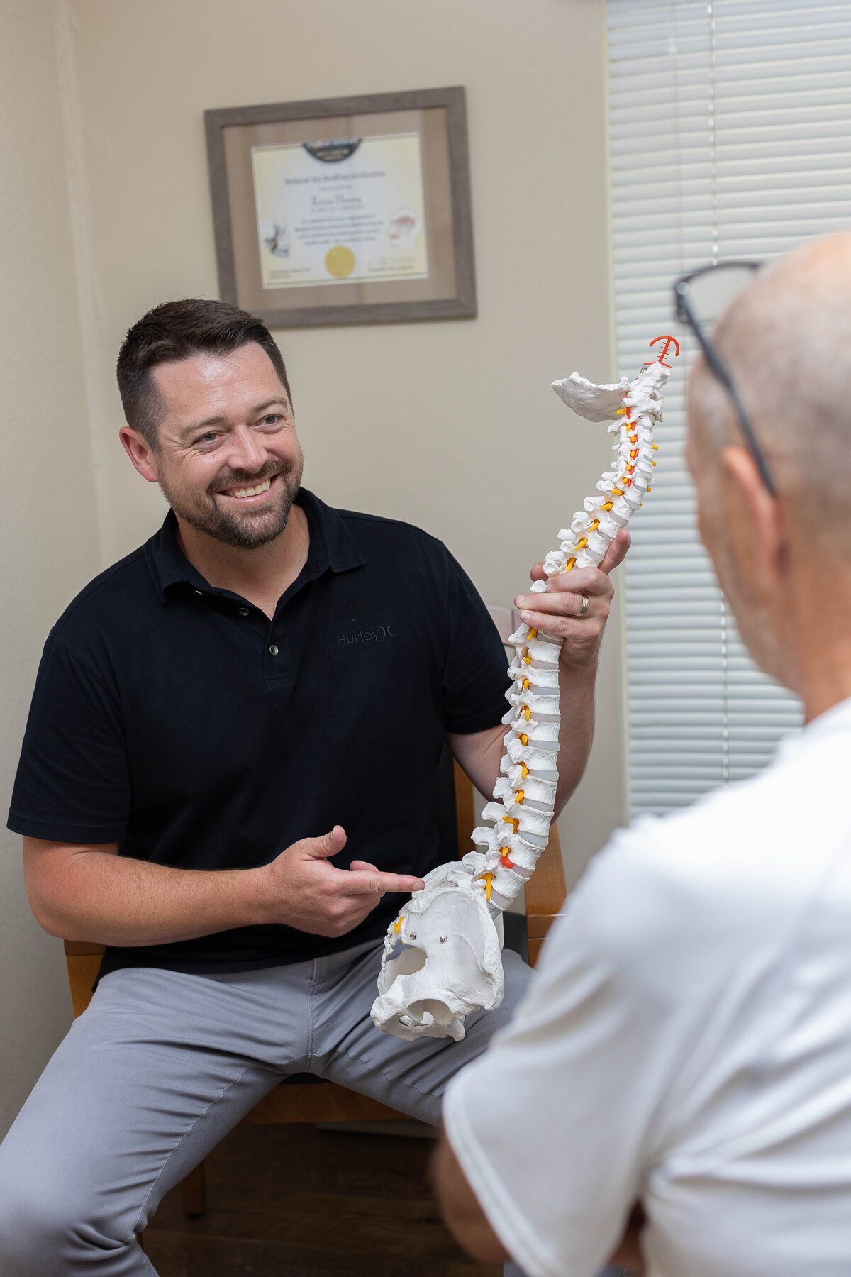 Smiling doctor showing a model of a spine to an older gentleman