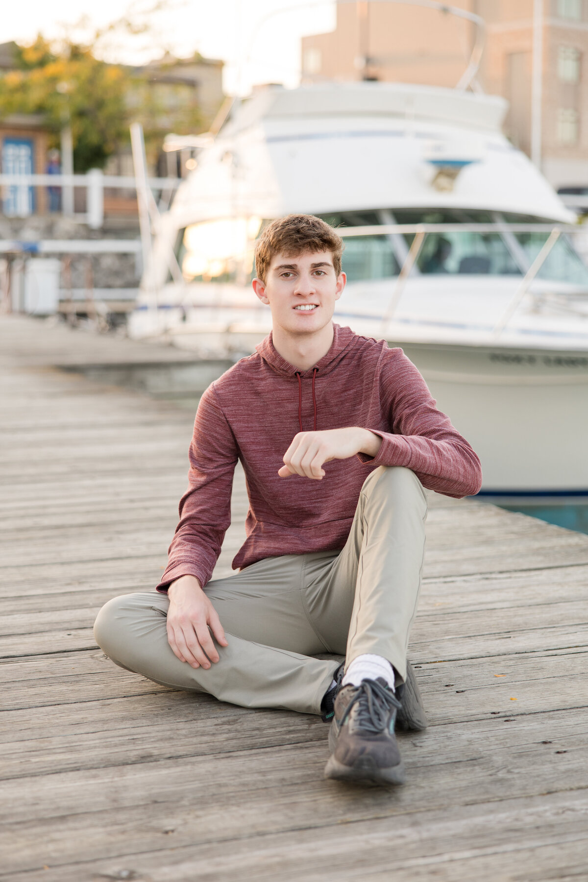 Senior guy seated on a pier in front of a boat, smiling at the camera