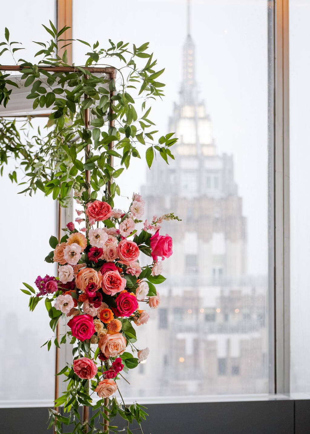 Romantic indoor wedding ceremony setup with a lush floral arch, floor arrangements, and city skyline backdrop