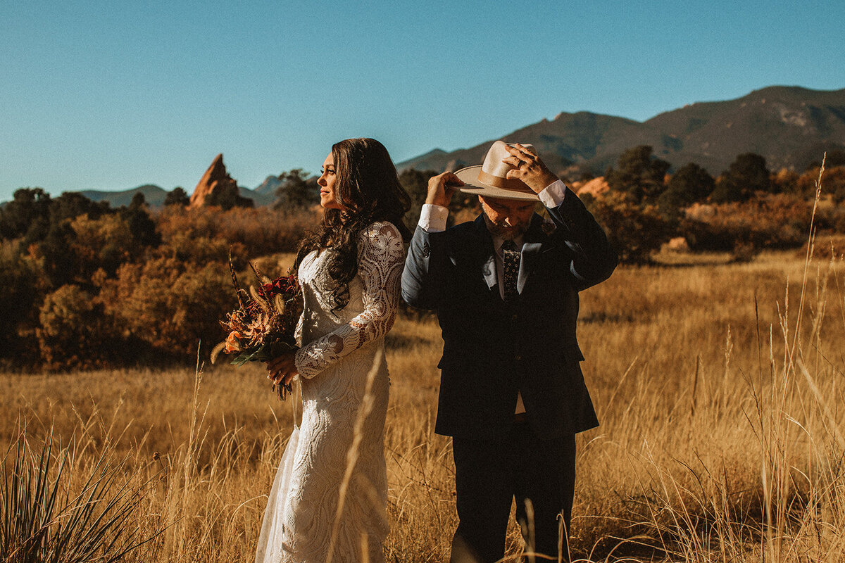 woman in wedding dress and man in suit stand in field at garden of the gods